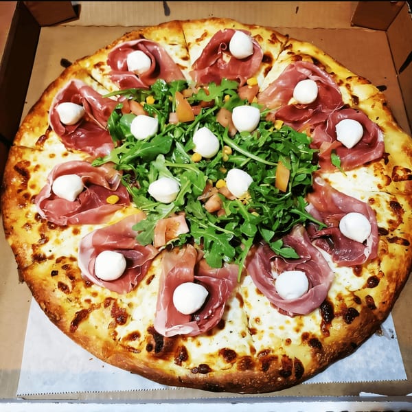 A whole Alessandro's Pizza with prosciutto, fresh mozzarella balls, and a vibrant arugula salad.