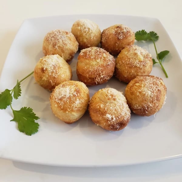 Nine golden-brown Italian arancini balls, sprinkled with Parmesan cheese and garnished with cilantro on a white plate.