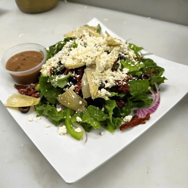 A fresh Italian salad with lettuce, artichokes, sun-dried tomatoes, feta, and dressing on a white plate.