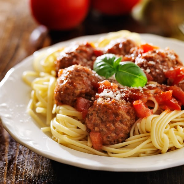 A plate of spaghetti and meatballs with tomato sauce, parmesan cheese, and basil.