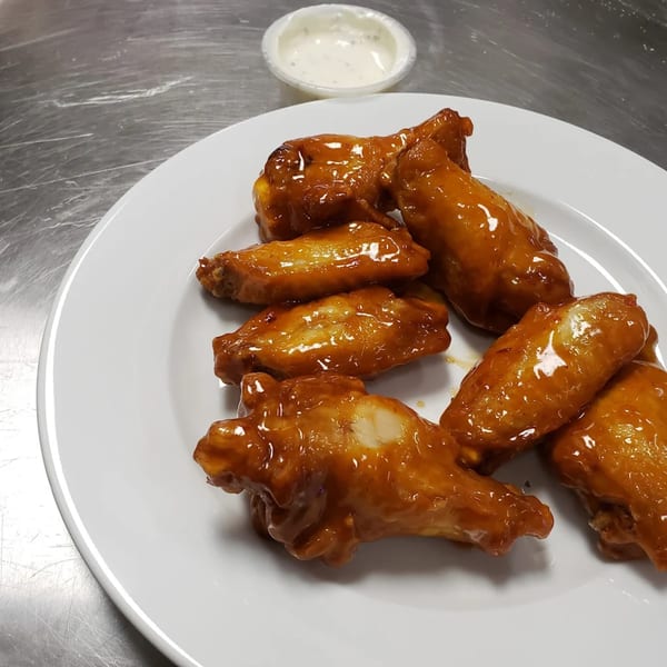 A white plate holds several glossy, brown chicken wings with a side of ranch dressing.